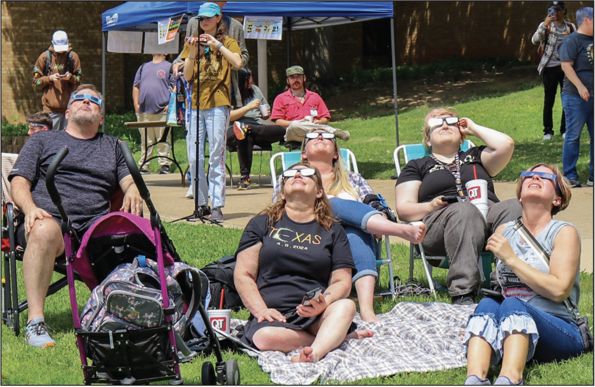 NE community members gather together to look at the eclipsing sun above them using safety glasses for viewing.